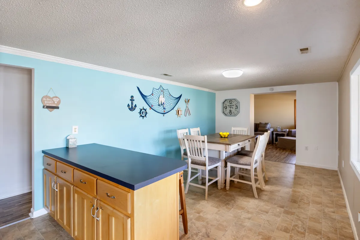 A cheerful dining area with a blue accent wall featuring nautical decor, a dining table adorned with fresh yellow flowers, and the kitchen island in view. The mood is relaxed and friendly, inviting families to gather and make memories.