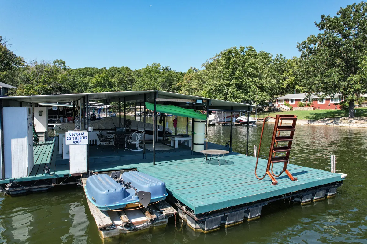 A vibrant dock scene featuring boats, a water slide into the lake, and a seating area for relaxing. The dock is equipped for boating, swimming, fishing, and lounging, with visible activity equipment and easy access to the water.