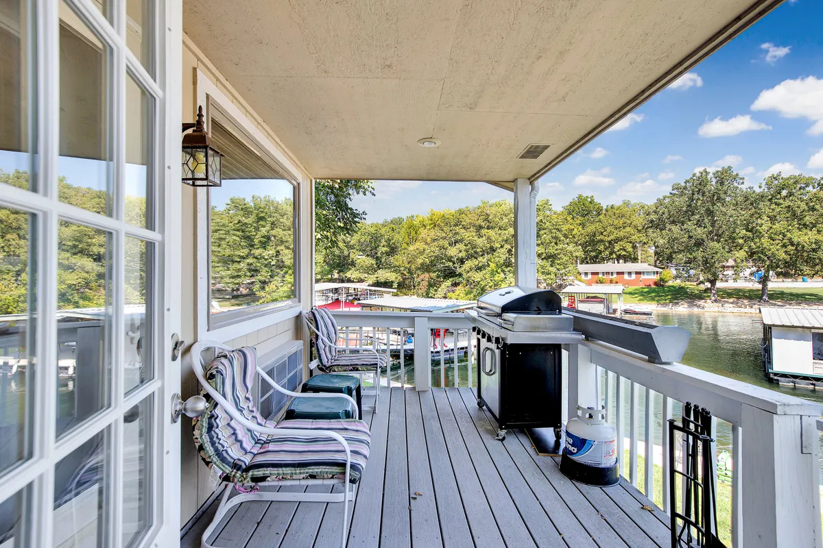An inviting exterior shot featuring a grill, outdoor seating area, and a stunning water view framed by leafy trees. The setup is ideal for outdoor dining, socializing, and enjoying meals together while overlooking the lake.
