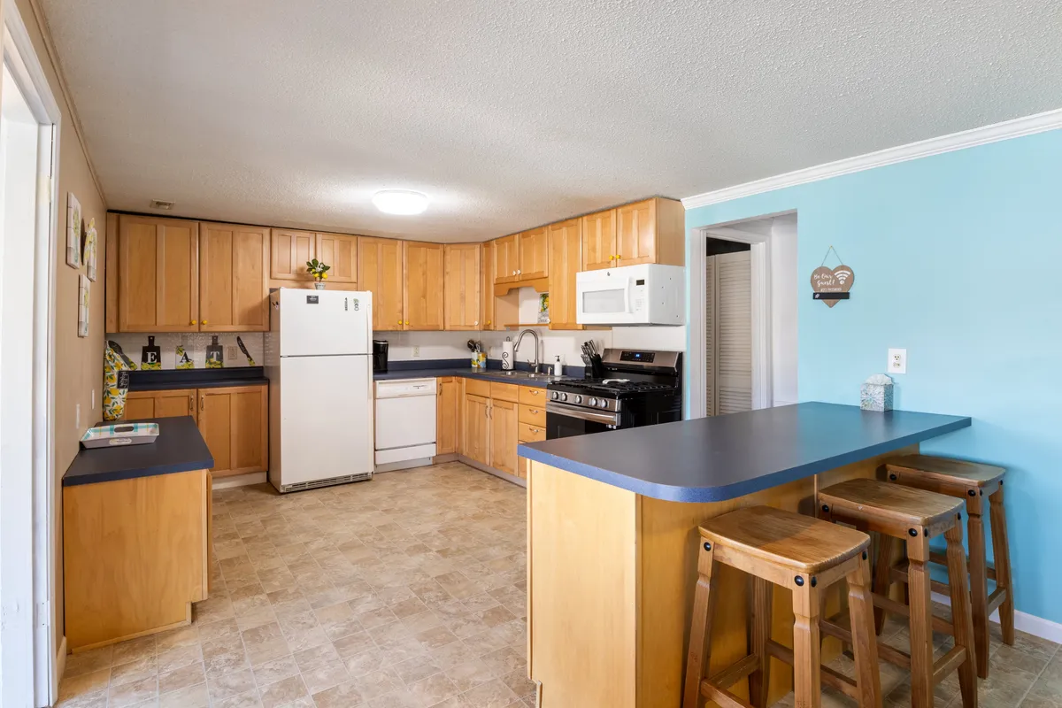 This image features a warm and welcoming kitchen with a central island, wooden cabinetry, and white appliances. The space is designed for cooking, gathering, and entertaining, with plenty of counter space for meal prep and social interaction.