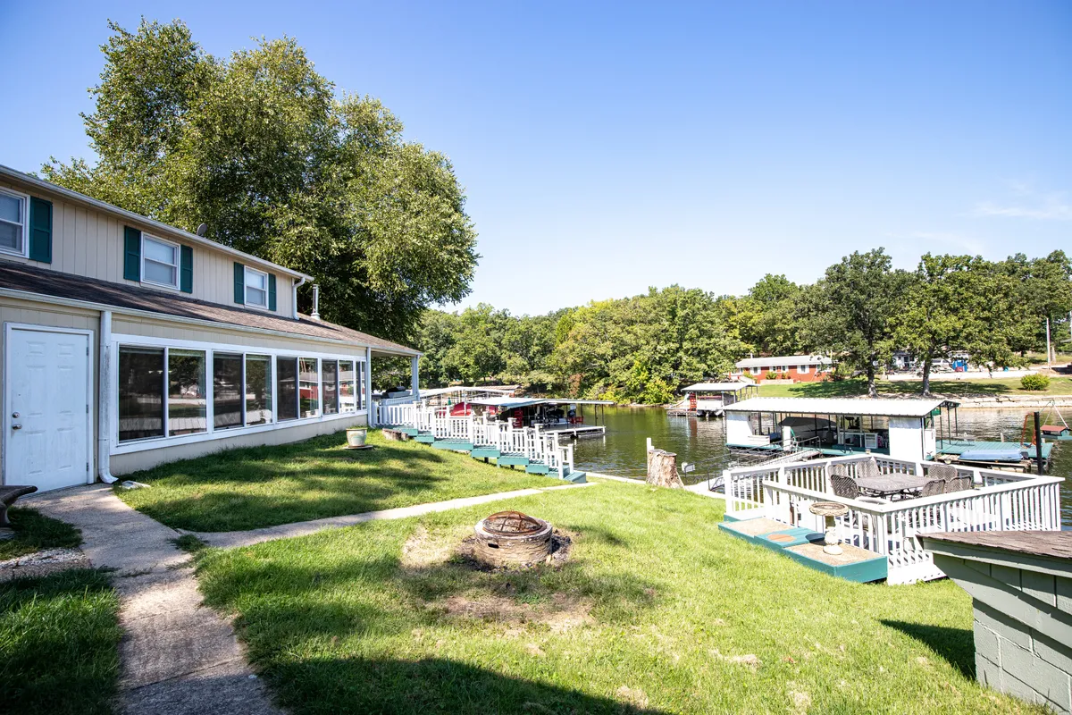 This exterior image showcases the private home nestled by the water, complete with visible boat docks and a fire pit area. The house is set against a beautiful lakeside backdrop, with greenery all around and ample space for outdoor activities.