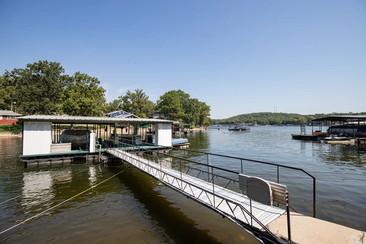 A tranquil scene featuring a dock extending over the water, surrounded by boats and lush greenery. The area is ideal for fishing, kayaking, and relaxing by the lake, with a calming, recreational vibe perfect for all ages.