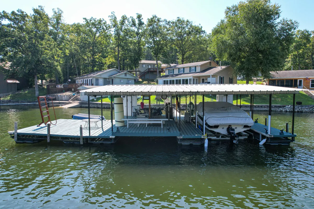 A spacious dock with a boat moored alongside, surrounded by trees and with inviting seating areas. The background features lakeside houses, creating a welcoming space for both active and relaxing moments.