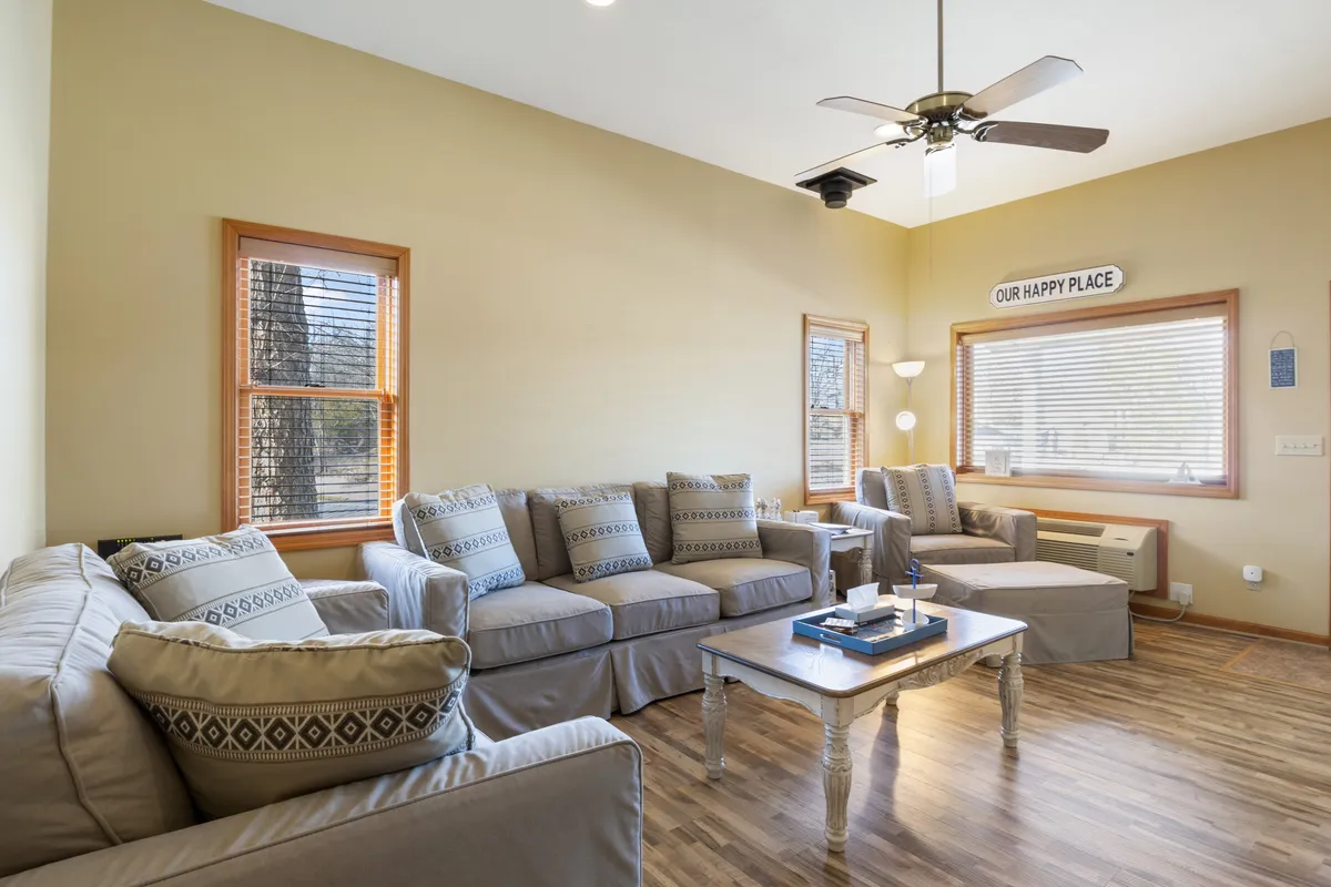 A cozy, open-plan living room featuring a plush sofa set, a coffee table, and a window streaming in natural light. A decorative sign reading 'OUR HAPPY PLACE' and other homey touches create an inviting atmosphere perfect for family gatherings or relaxing afternoons.